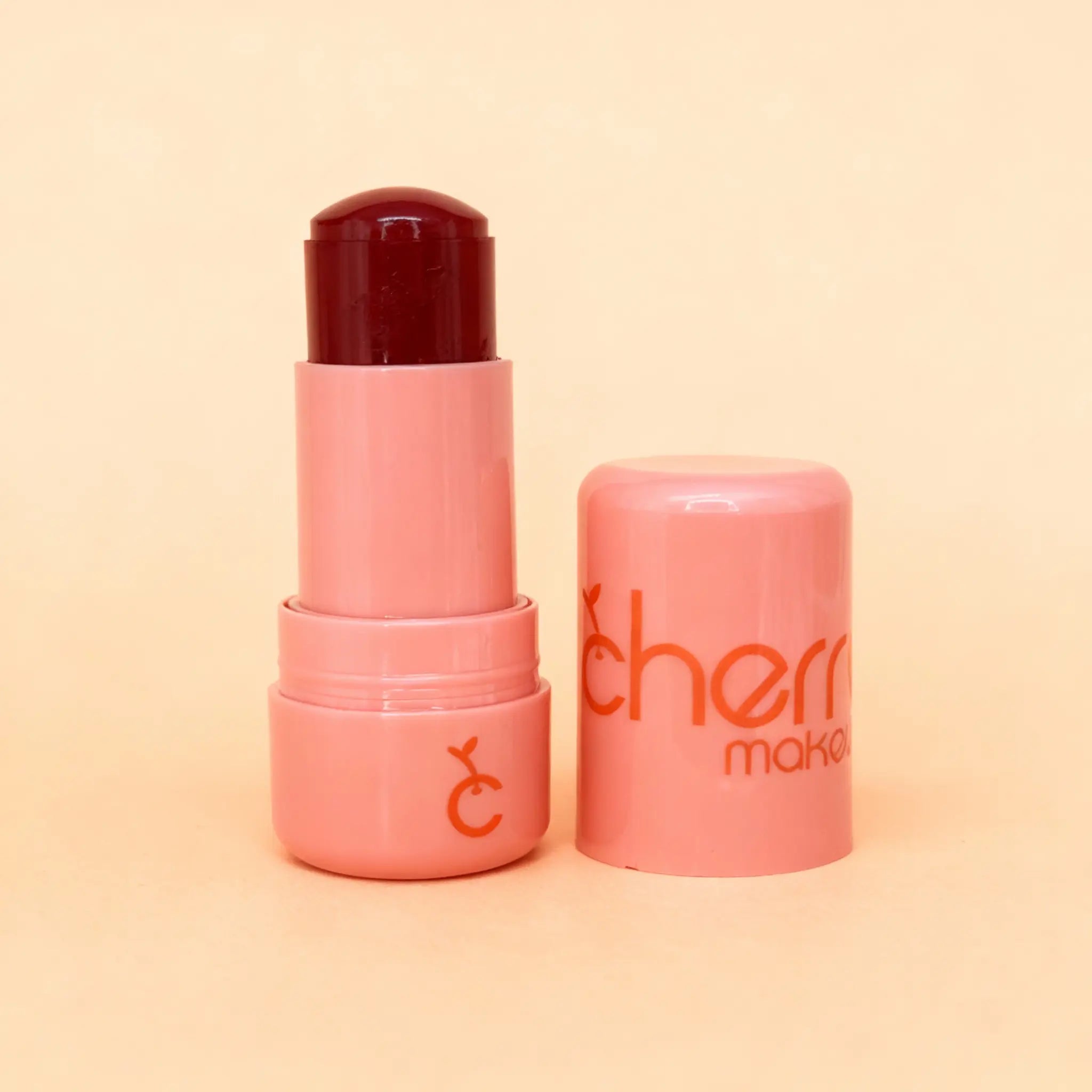 Pink lip balm with dark red cap on a peach background