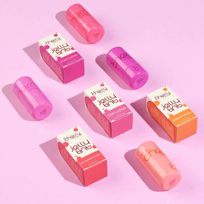 Pink and orange lip glosses with their packaging on a pink background