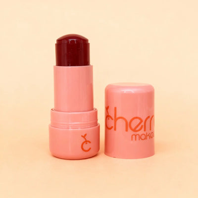 Pink lip balm with dark red cap on a peach background